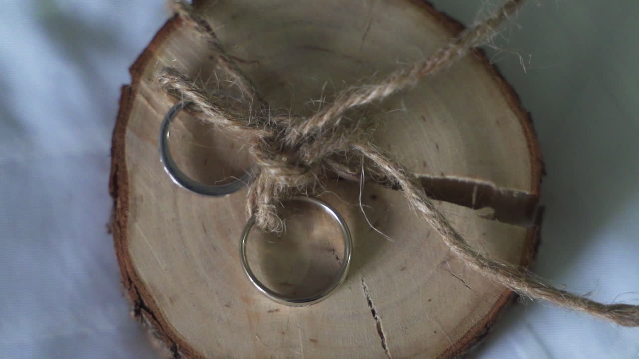 Two gold with diamonds wedding rings bands on round slice of live edge wood tied together with brown twine