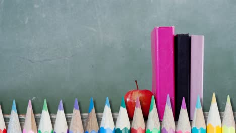 varios lápices de colores contra la manzana y libros en superficie de madera contra la pizarra