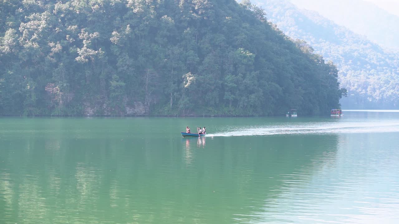 A three manned boat paddling fast to return to the shore of the Fewa Lake, Pokhara