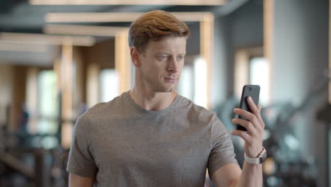 Confident-athlete-man-having-video-call-in-sport-club.-Sportsman-standing-at-gym