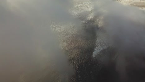 Aerial-landscape-view-going-through-clouds,-over-the-textured-ice-surface-of-an-icelandic-glacier