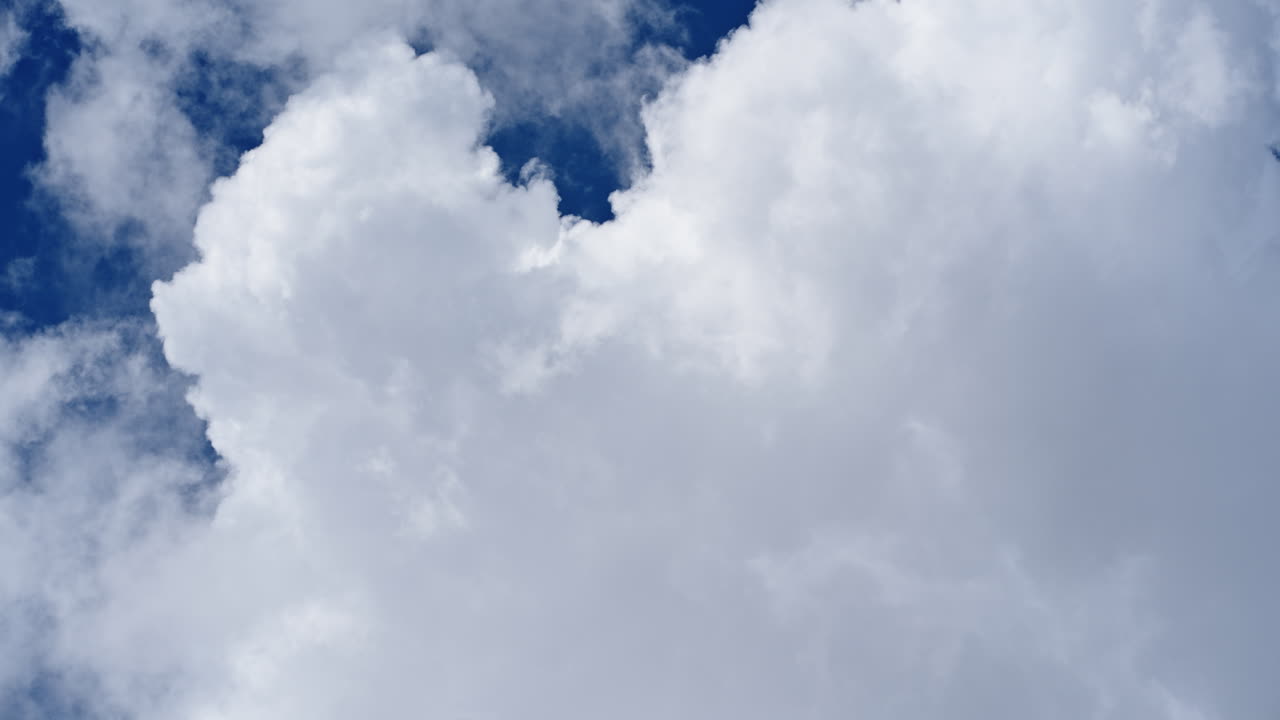 Fluffy white clouds grow and shift in a fast-moving sky timelapse scene
