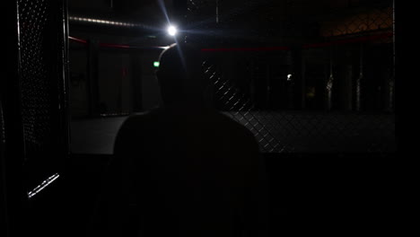 Zeitlupe-Eines-MMA-Kämpfers,-Der-Einen-Ring-Betritt-Und-Sich-Dann-Auf-Einen-Kampf-Vorbereitet,-Der-Seitlich-In-Einem-Dunklen-Raum-Mit-Einem-Einzigen-Licht-Im-Hintergrund-Läuft