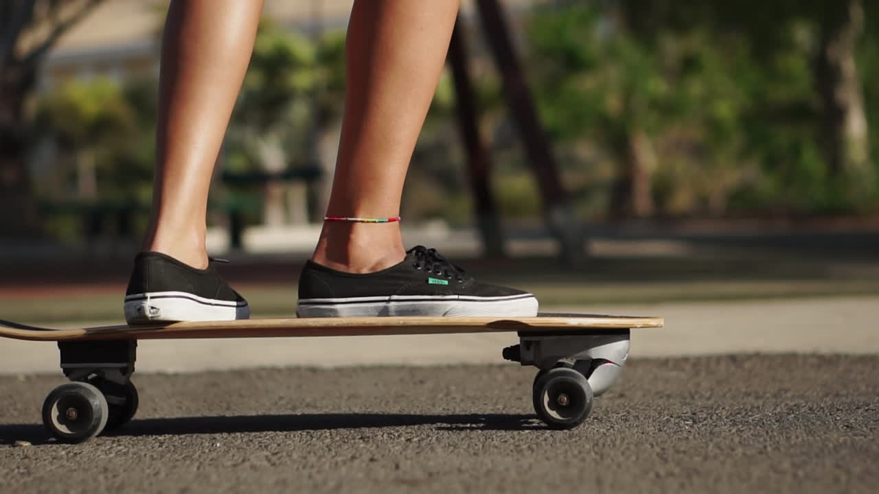 Slow motion frames a young woman's longboard journey near palm trees, her summer attire of shorts and sneakers adding to the allure