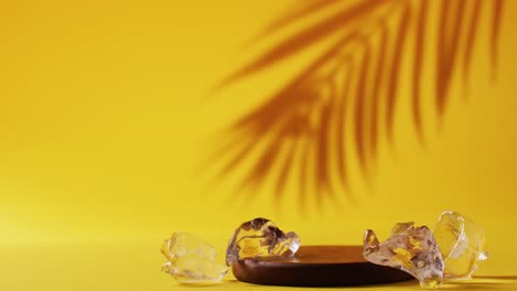 Close-up-of-ice-cubes-and-shadow-of-leaf-on-yellow-background