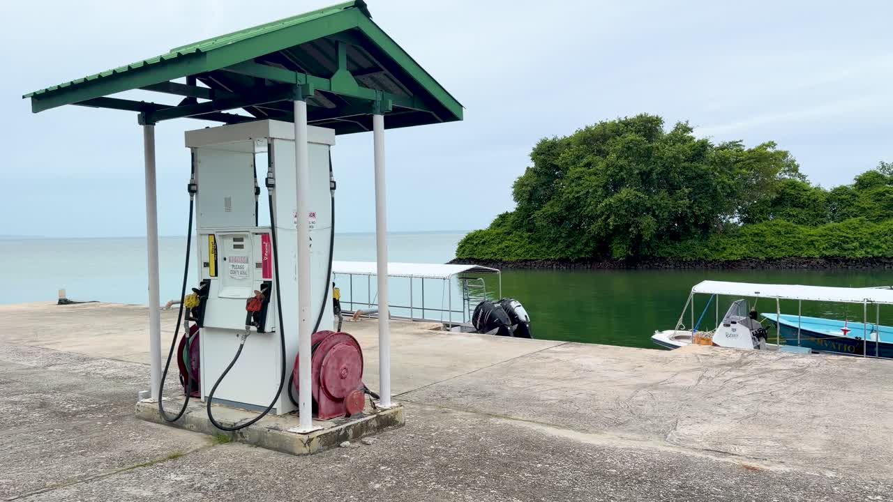 Static wide shot of a gasoline pump at a tropical marina pier under overcast skies