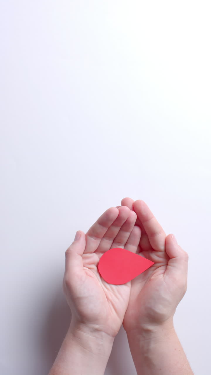 Vertical video of hands of caucasian man holding blood drop on white background with copy space