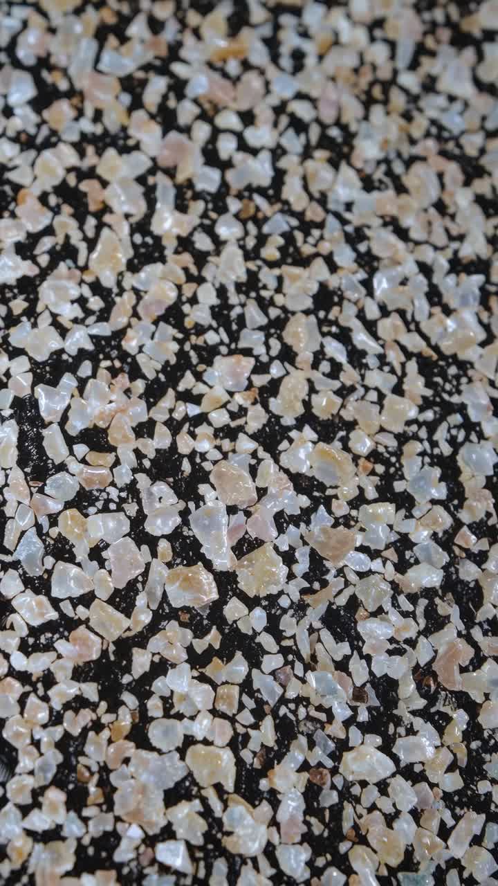 Close-up, top-down view of coarse salt crystals scattered on a dark surface, ideal for a texture