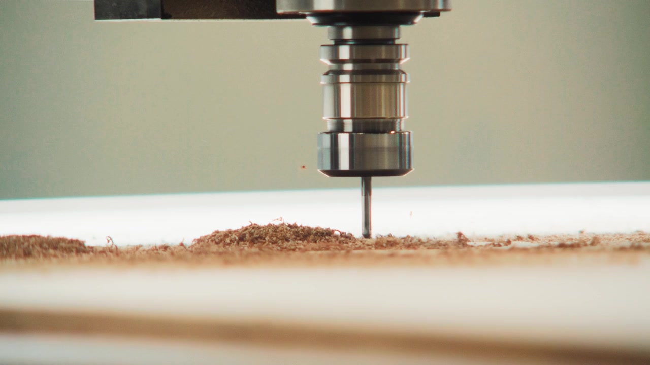 Macro di un mandrino CNC che taglia una tavola chiara con una linea di segatura fresca al rallentatore