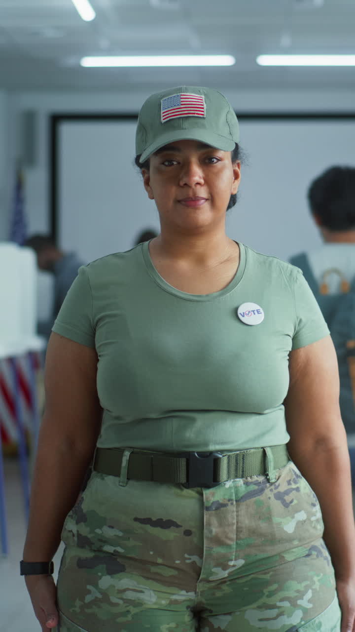 retrato de una mujer soldado, votante de las elecciones de los estados unidos de américa. una mujer en uniforme de camuflaje se para en la estación de votación y mira a la cámara. fondo con cabinas de votación. concepto de deber cívico.