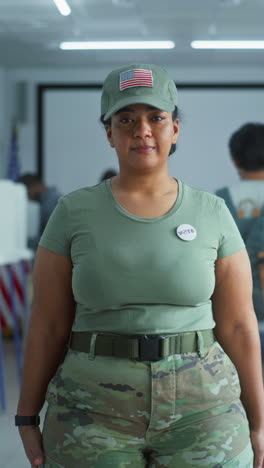 Portrait-of-female-soldier,-United-States-of-America-elections-voter.-Woman-in-camouflage-uniform-stands-in-polling-station-and-looks-at-camera.-Background-with-voting-booths.-Concept-of-civic-duty.