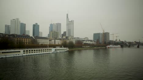 Vista-Nublada-Del-Horizonte-De-Frankfurt-Con-El-Río-Principal-Y-Los-Barcos-Que-Pasan,-Grúas-En-Los-Sitios-De-Construcción