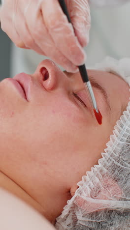 esteticista aplicando una máscara de crema hidratante química médica en el rostro de una mujer joven adulta