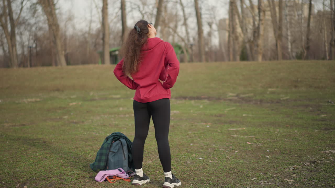 Athlete Prepares Outdoors, Sportive Woman In Hoodie Monitoring Park Surroundings Before Running, Young Female Athlete In Comfortable Clothing Attentively Observing Area Before Beginning Exercise