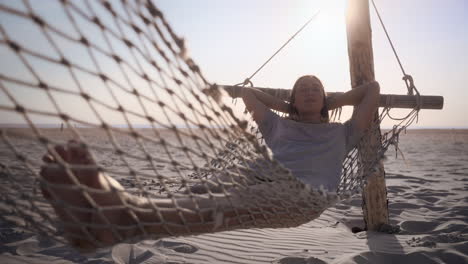 young woman relaxes in a hammock at the beach on a sunny day