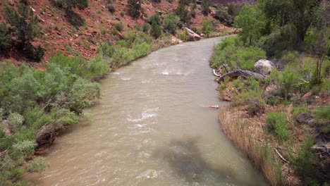 Tilting-up-shot-of-a-small-desert-river-flowing-through-a-canyon-at-Zion-National-Park