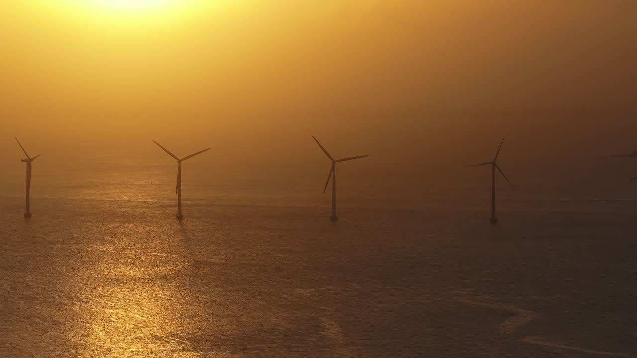 Aerial drone view of the golden sun over the Danish coast, casting light on offshore wind turbines