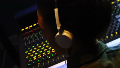 male audio engineer listening to headphones while mixing sound