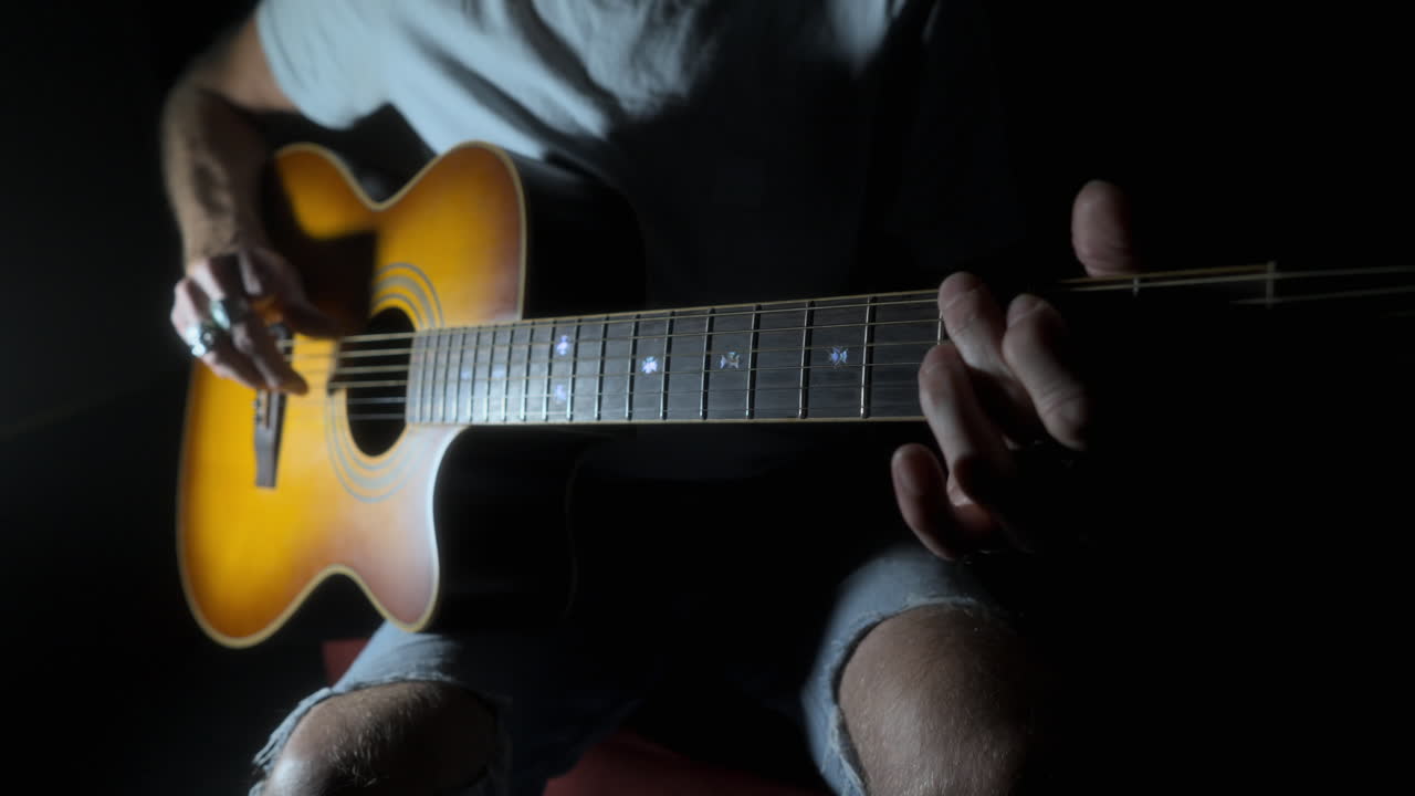 hombre con dedos faltantes tocando la guitarra acústica en una fuerte iluminación de mal humor