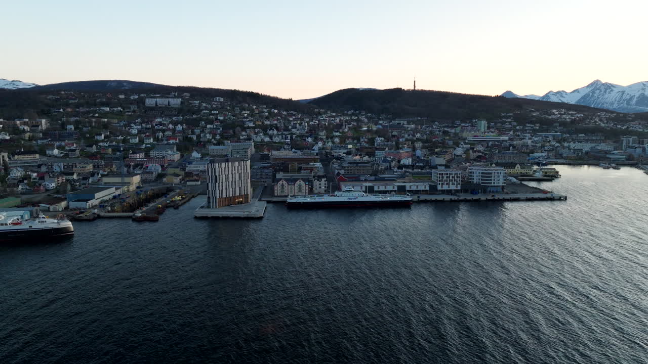 Scenic aerial drone view of Harstad waterfront in Northern Norway. Panoramic view of the city skyline, harbor, and distant snowy mountains. Ideal for travel and Scandinavian tourism content