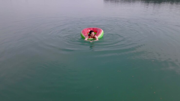 overhead top view of woman swimming with watermelon swimming circle in blue water