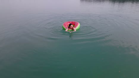 overhead top view of woman swimming with watermelon swimming circle in blue water