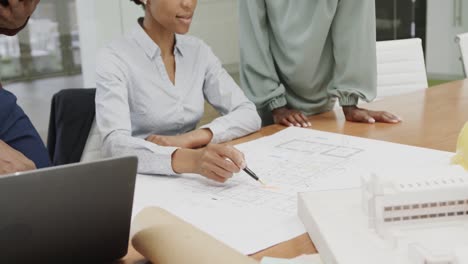 african american male and female architects discussing blueprints in office in slow motion