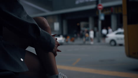 woman legs sitting city background on bus stop near crowded street.