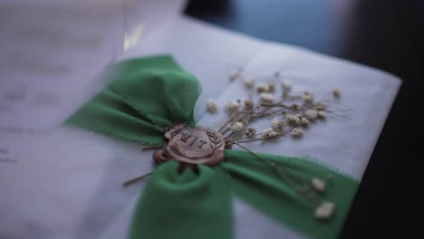 close up of a wedding invitation sealed with green ribbon, wax stamp, and dried flowers