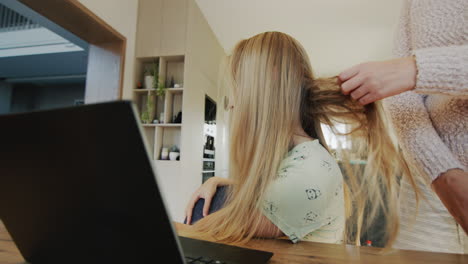 Woman-trying-to-untangle-her-teenage-daughter's-long-hair.-Side-view