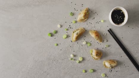 composición de albóndigas de gyoza y salsa de soja con palillos sobre fondo gris