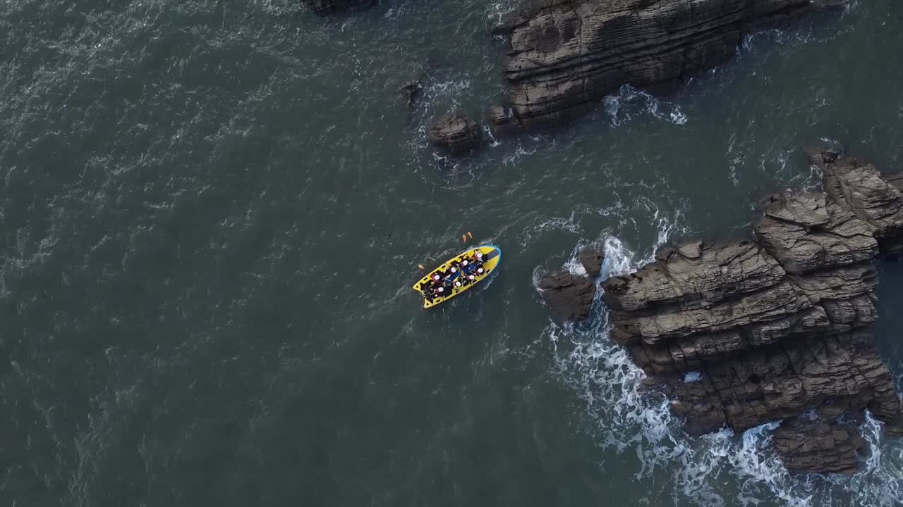Vista aerea con drone di persone su un paddleboard giallo per più persone che navigano tra le rocce lungo la costa sotto una scogliera rocciosa - Lee Bay, Beach, Ilfracombe, Devon, Inghilterra.