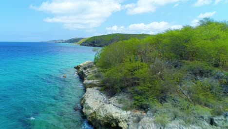 drone flies over bleached white rocky cliff and shrubs to san juan beach curacao