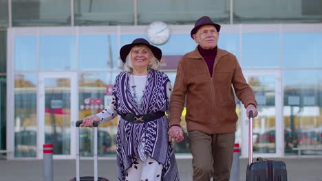 turistas jubilados abuela abuelo caminando desde la sala del aeropuerto con equipaje en ruedas