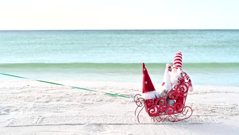 christmas gnome on the beach in a red sled on a sunny winter day