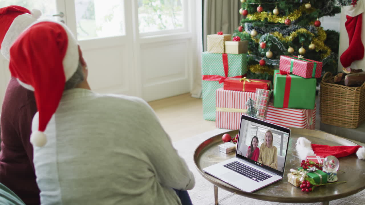 diversas amigas mayores que usan una computadora portátil para una videollamada de navidad con una familia feliz en la pantalla
