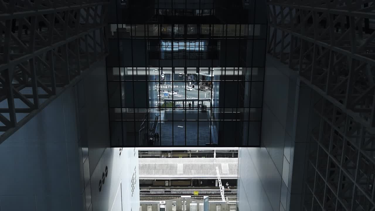 Framed urban view through the glass facade of Kyoto Station, overlooking train platforms and a busy city intersection in Kyoto, Japan.