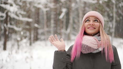 Slow-motion,-winter-woman-in-the-woods-watching-the-snow-fall-and-smiling-looking-at-the-sky-and-directly-into-the-camera.