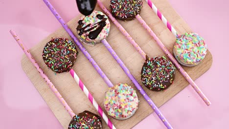 decorating delicious sweet cake pops on wooden board with melted black chocolate