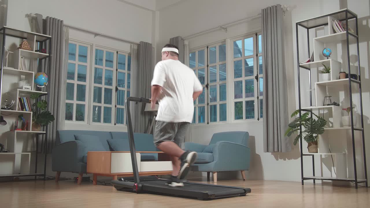 Back View Of Asian Fat Man Running On A Treadmill At Home