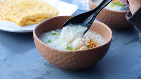 person garnishing porridge with green onions and crispy toppings