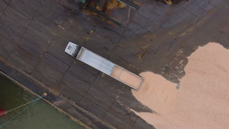 aerial birdseye view of wood terminal, truck unloading wood chip cargo into the large pile, port of liepaja , lumber log export, overcast day with fog and mist, orbiting drone shot