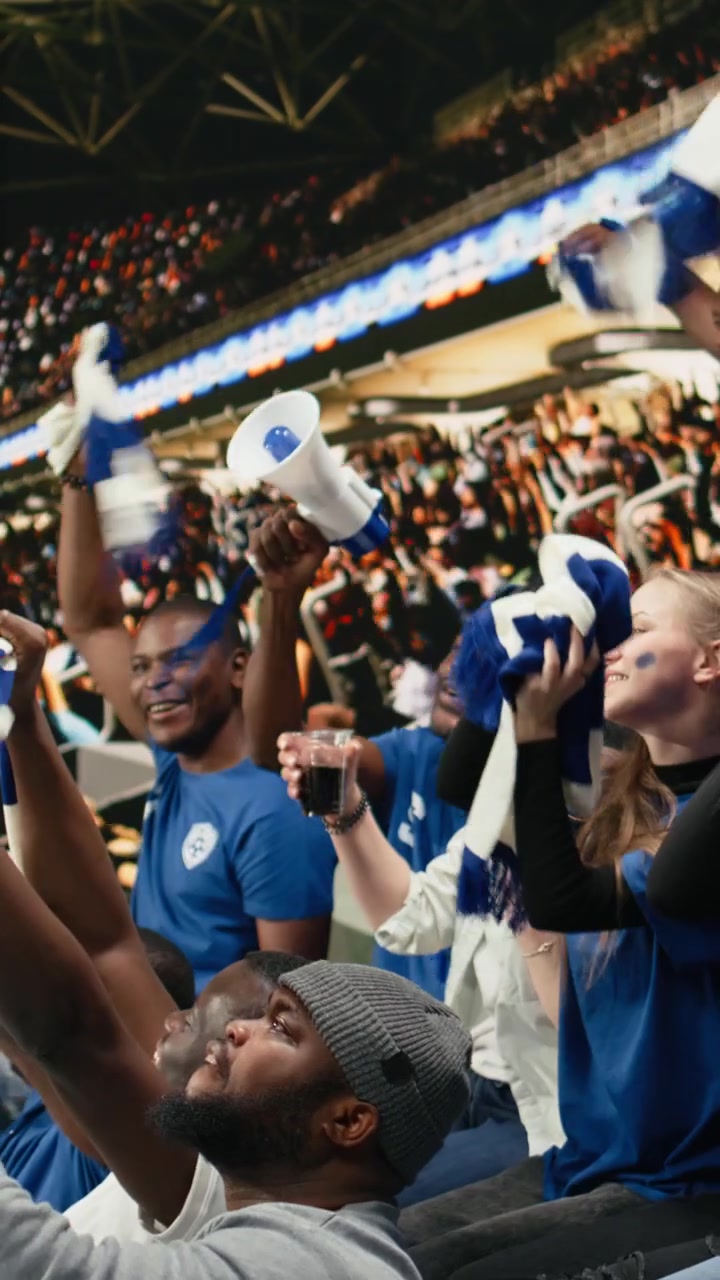 Video vertical: Entusiasta aficionado al fútbol soplando una vuvuzela azul en la grada del estadio.