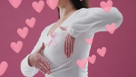 Animation-of-hearts-over-caucasian-woman-with-pink-ribbon-on-pink-background