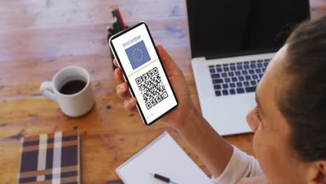 mujer en el escritorio con un teléfono inteligente con certificado de vacunación contra la covid, bandera de la ue y código qr en la pantalla