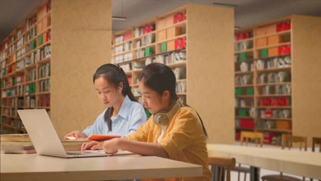 asian woman students with headphones reading books while sitting on the table with laptop in the library