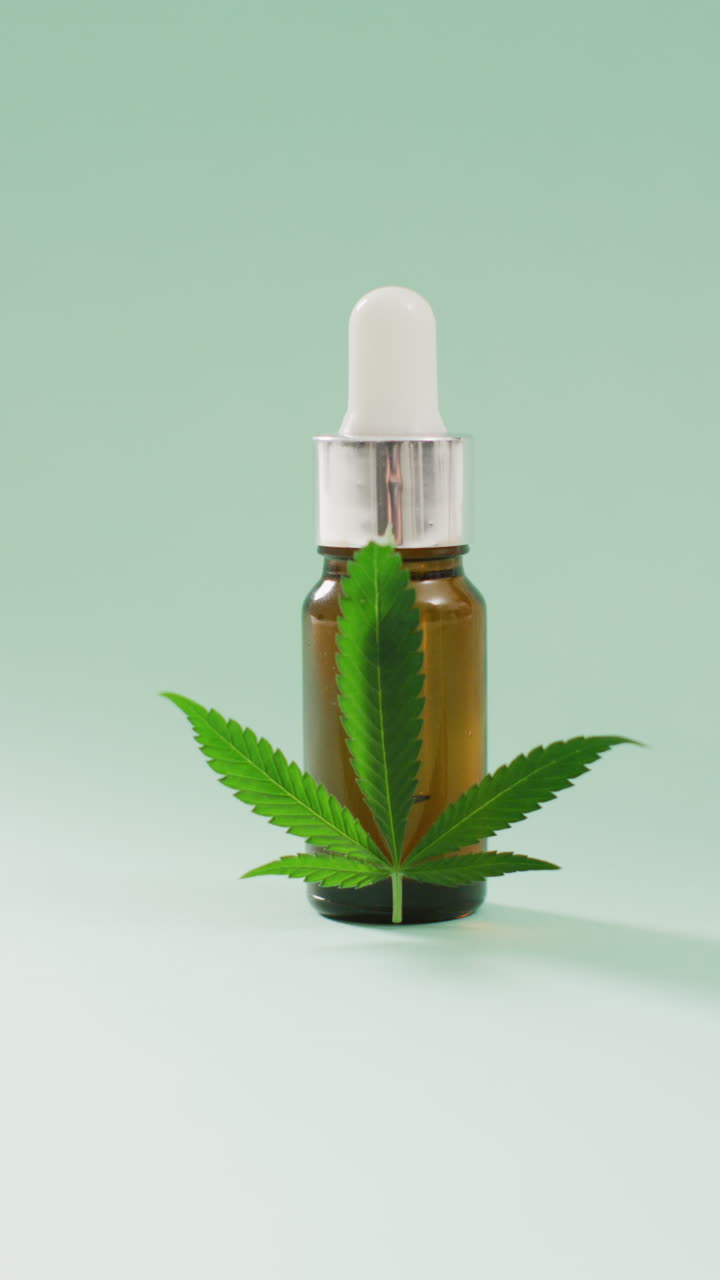 video verticale di foglia di marijuana e bottiglia di estratto di cbd su sfondo blu