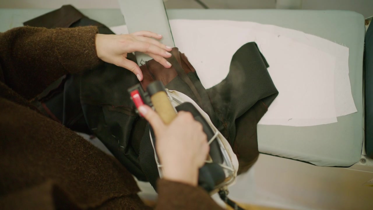 Primer plano de un sastre utilizando una plancha de vapor profesional sobre tela negra en un taller de moda.