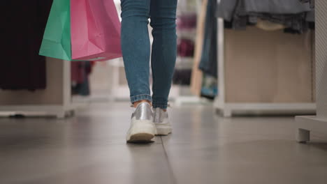 leg view of shopper walking through retail clothing store aisle carrying colorful shopping bags in vibrant modern environment with neatly arranged racks