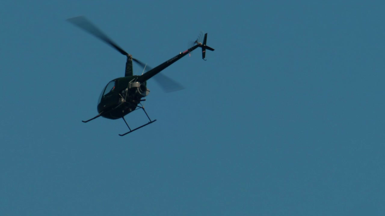 Helicóptero verde escuro voando por um céu claro de dia, com os rotores borrados pelo movimento. Conceito de aviação e viagem, Antibes, França.